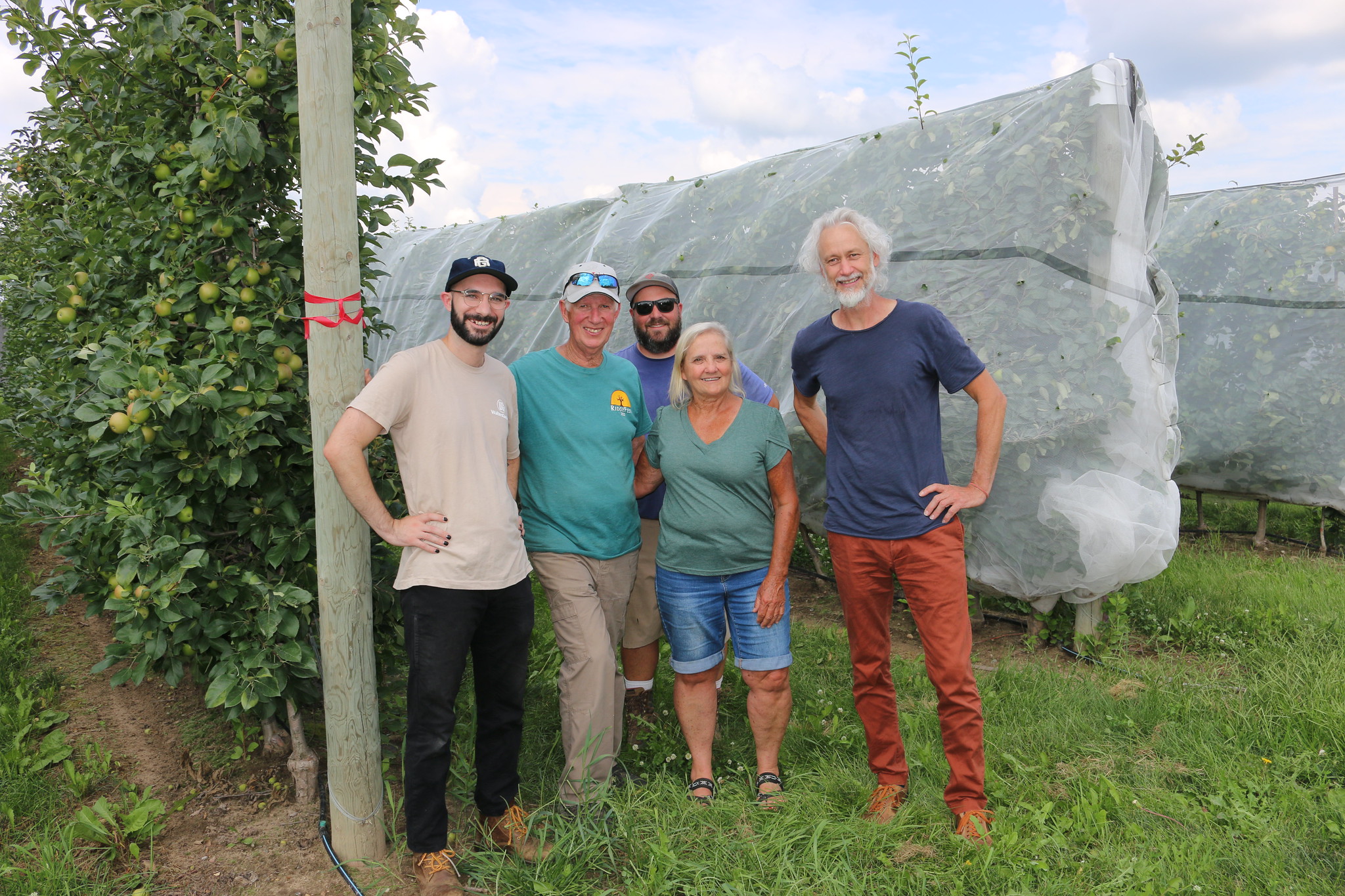 five people standing in front of apple trees