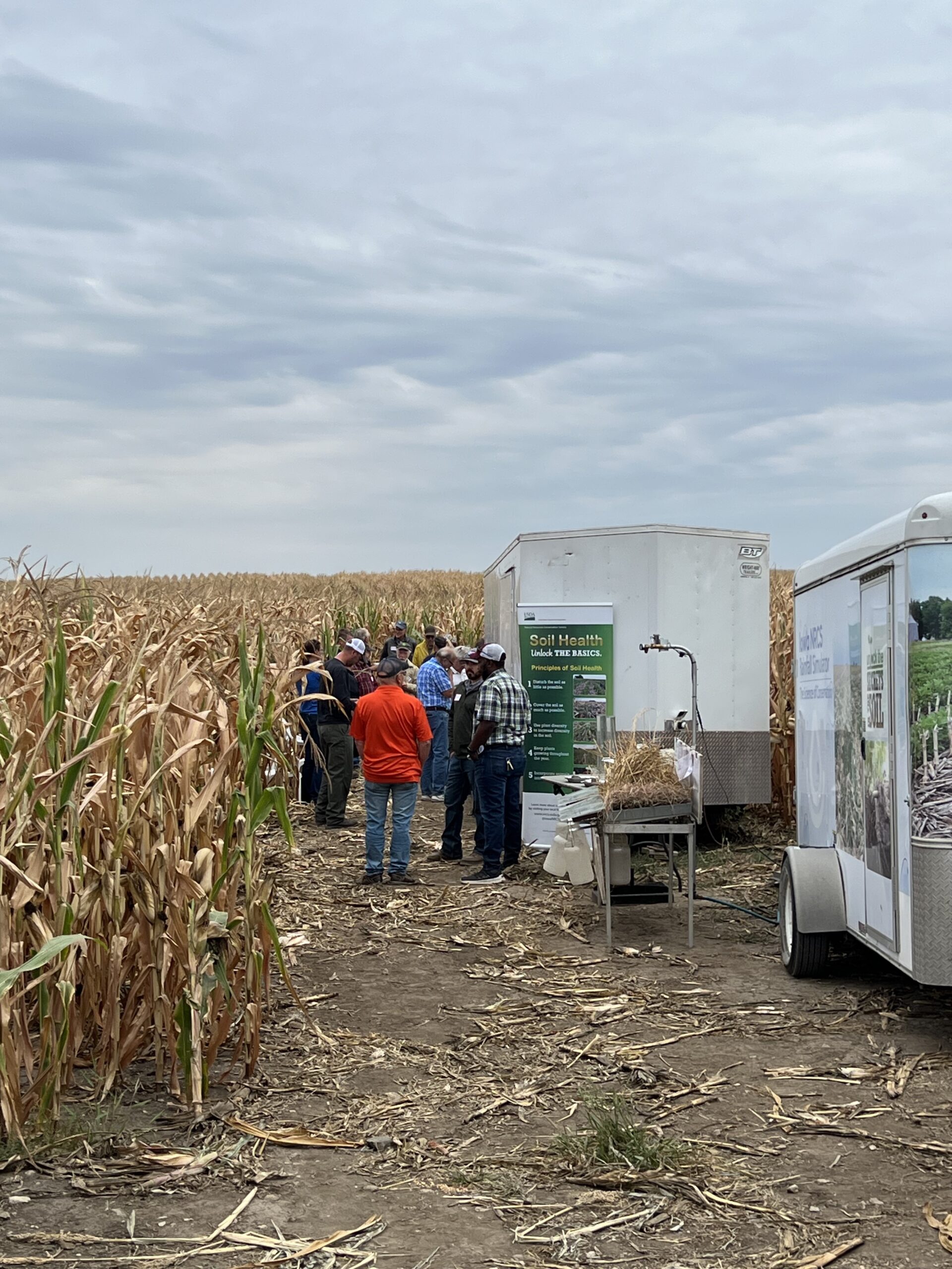 several people gathered for a field day in a corn field at harvest time