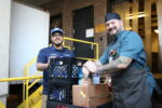 Two men standing by crates with cans of beans