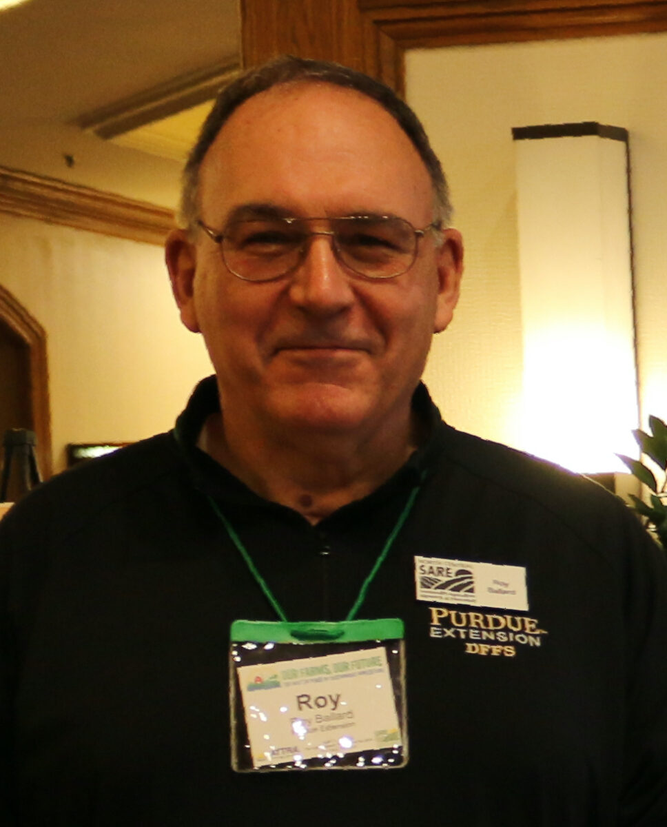 Roy Ballard wearing a SARE and NSAC name tags in a building