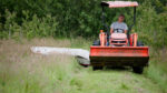a farmer in a tractor mowing a field of hay