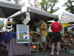 People standing outside of farmers market tents with the sign "Farmers Tailgate Market"